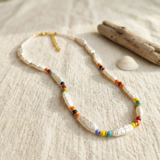 Necklace with colorful beads on a textured surface with driftwood and a shell.