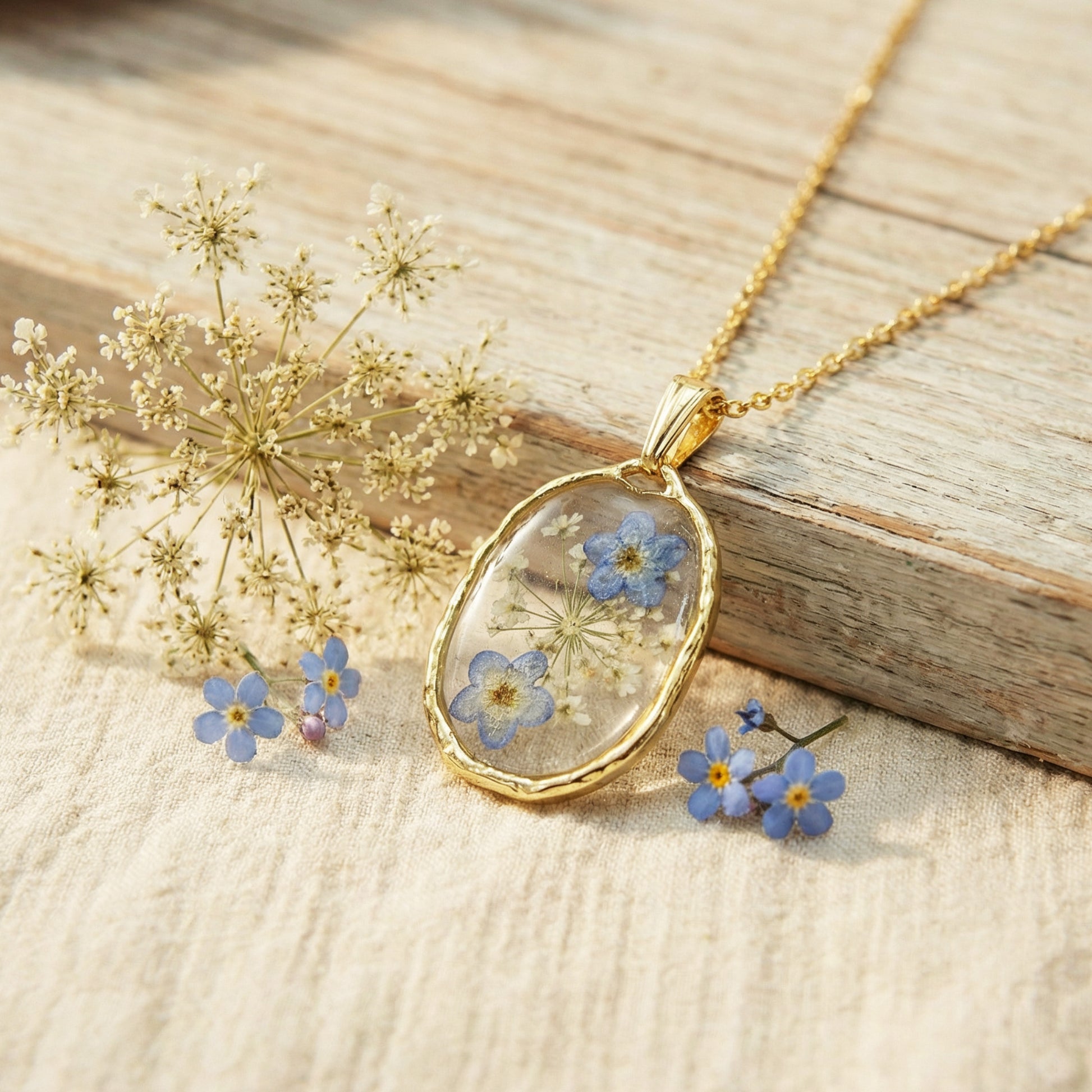 Gold necklace with a pendant featuring dried blue flowers on a wooden surface.