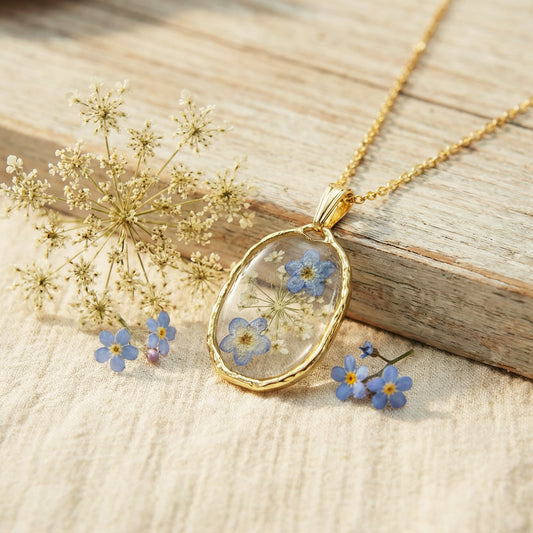 Gold necklace with a pendant featuring dried blue flowers on a wooden surface.