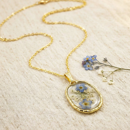 Gold necklace with a pendant featuring pressed flowers on a beige fabric background