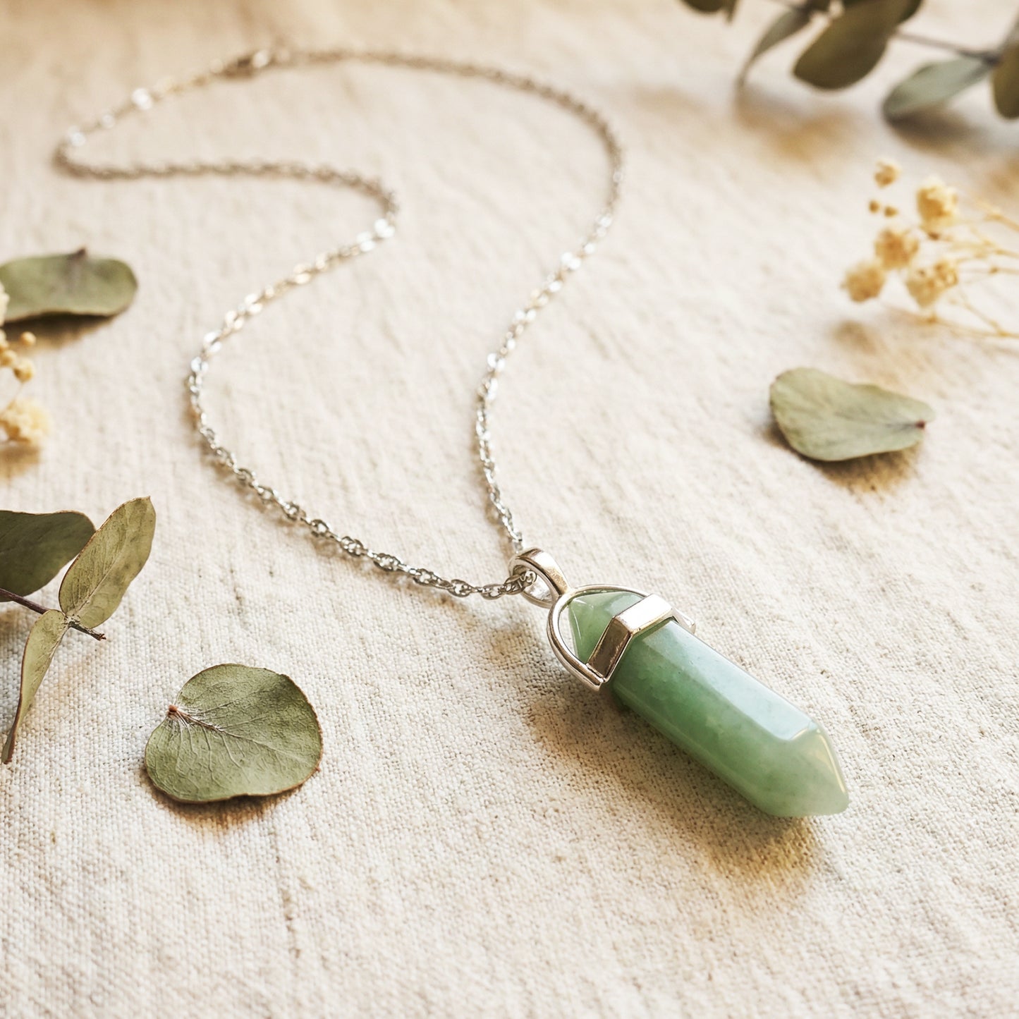 Necklace with a green pendant on a textured surface with leaves and flowers.