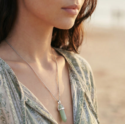 Woman wearing a necklace with a green pendant against a blurred background