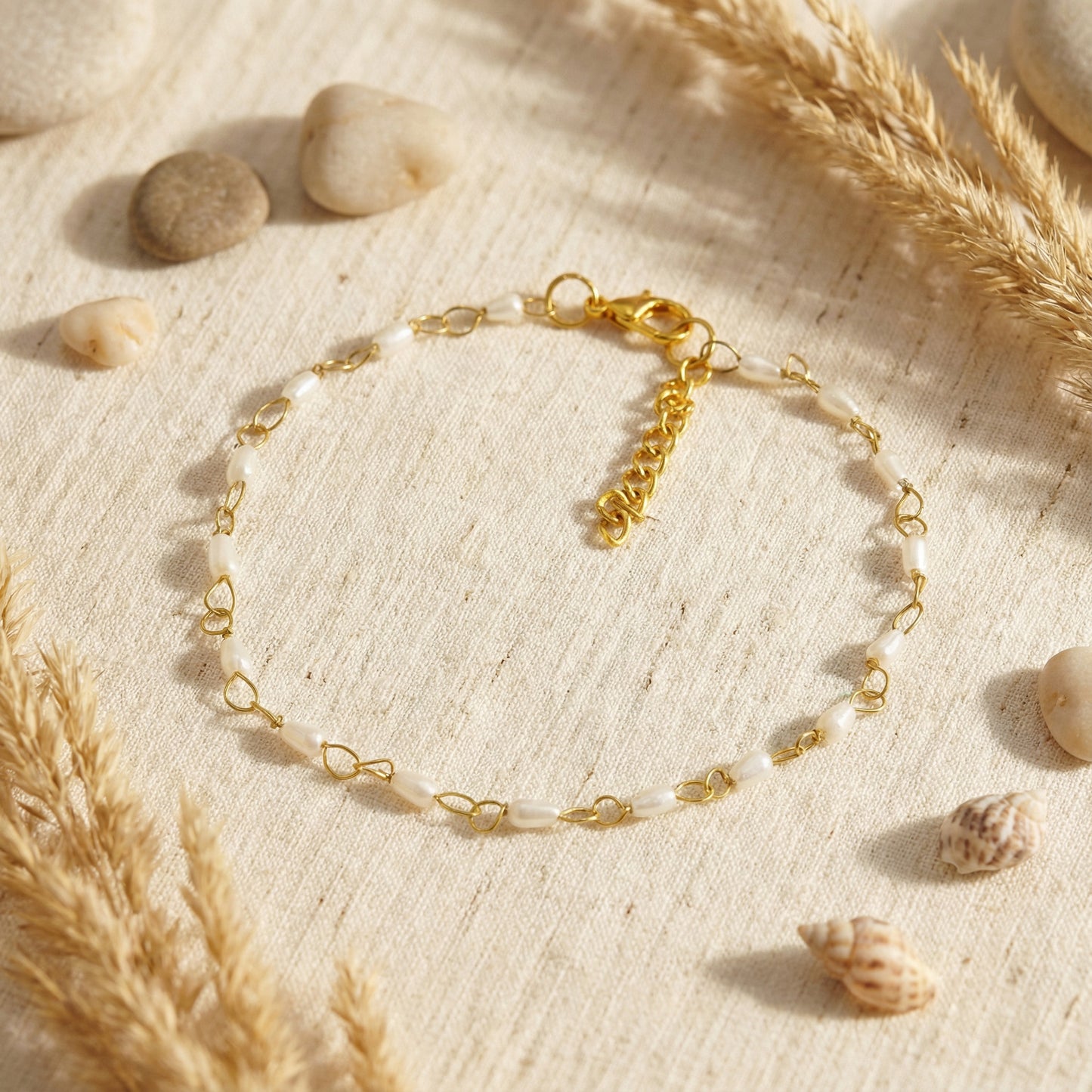 Gold bracelet on a textured beige surface with stones and pampas grass