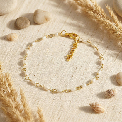 Gold bracelet on a textured beige surface with stones and pampas grass