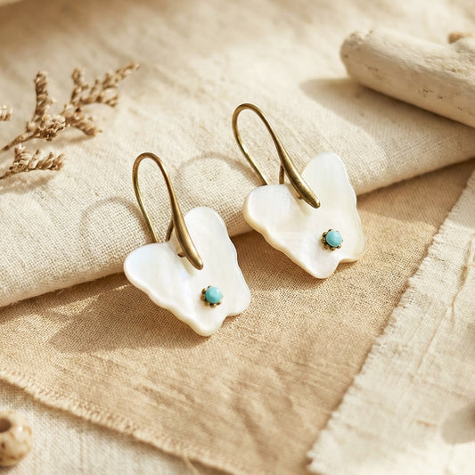 Pair of white earrings with turquoise stones on a beige fabric background