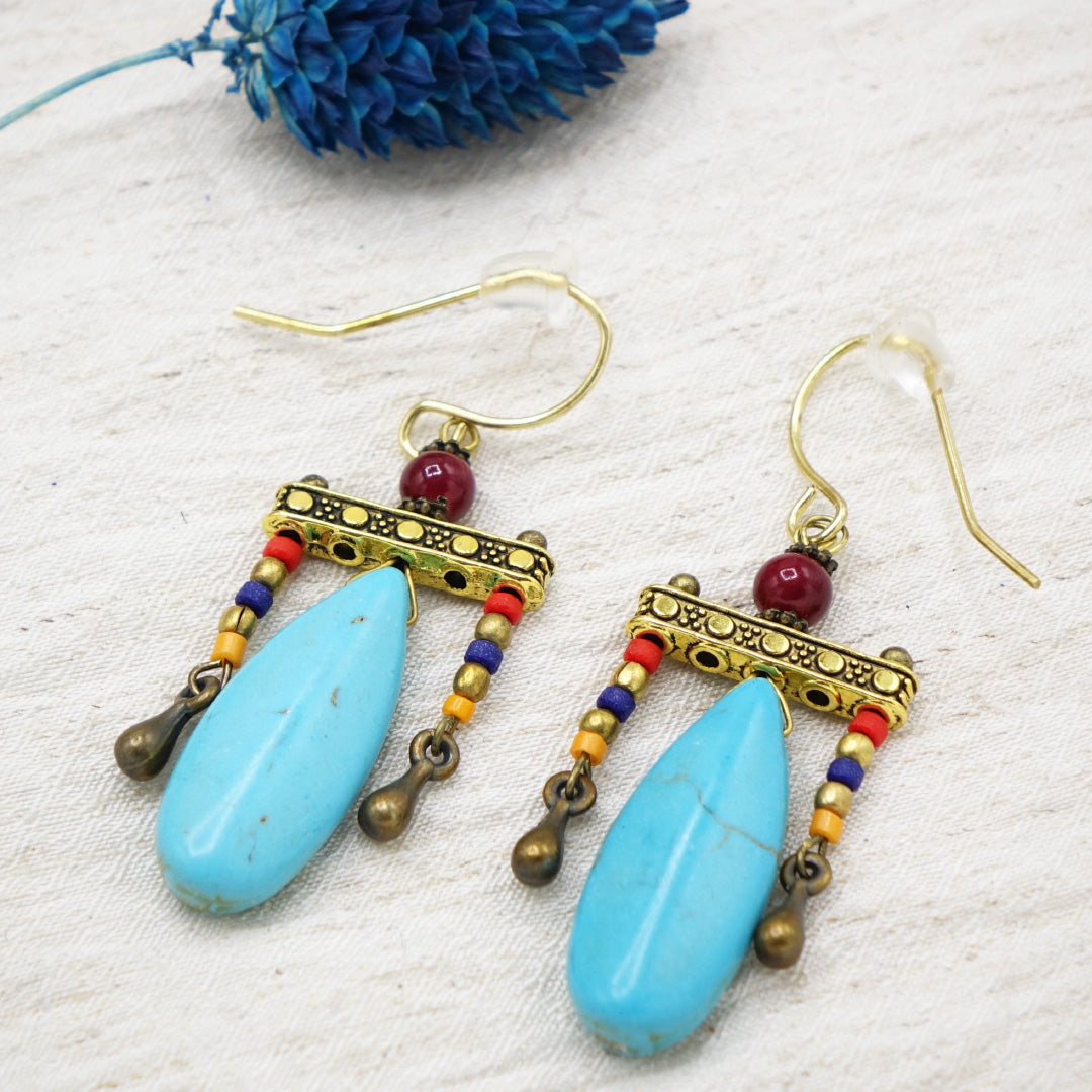 Pair of earrings with blue teardrop pendants and colorful beads on a textured white surface.