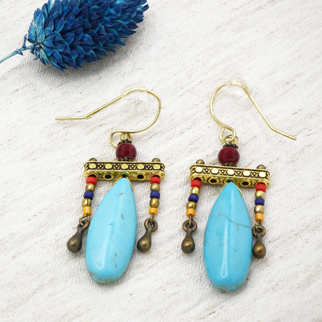 Pair of earrings with blue teardrop beads and gold accents on a textured white surface.