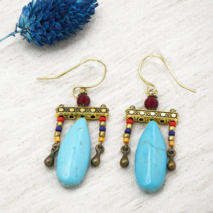 Pair of earrings with blue teardrop beads and gold accents on a textured white surface.