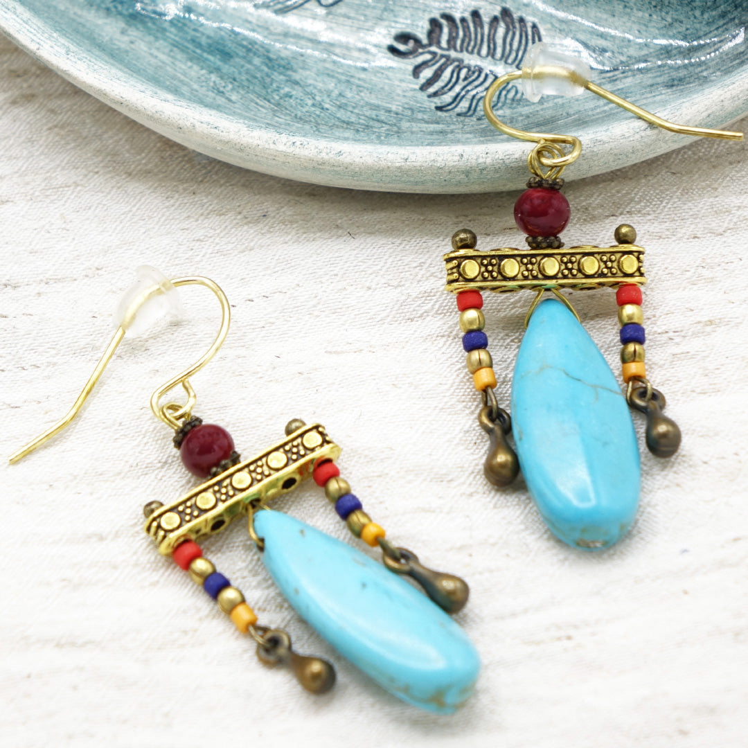 Colorful beaded earrings with turquoise stones on a textured surface.