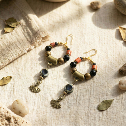 Pair of beaded earrings on a textured fabric surface with leaves and stones.