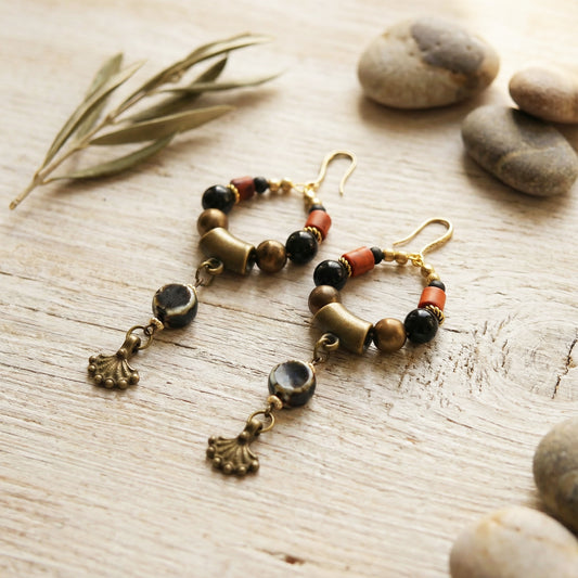 Pair of beaded earrings on a wooden surface with stones and leaves.