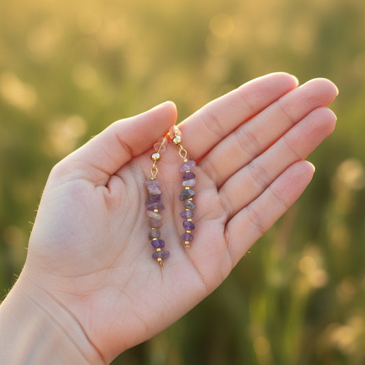 Hand holding two Amethyst Crystal Stone Earrings with a blurred natural background