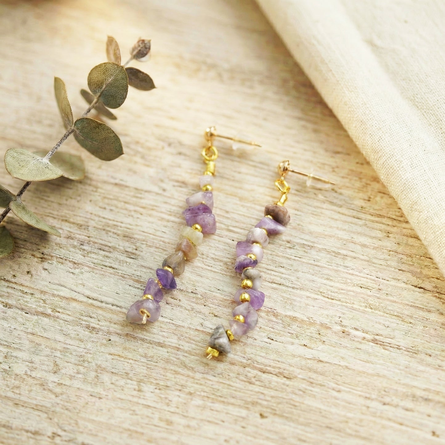 Pair of beaded earrings on a textured surface with green leaves