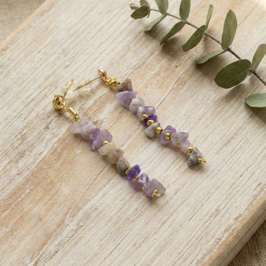Purple beaded earrings on a wooden surface with green leaves.