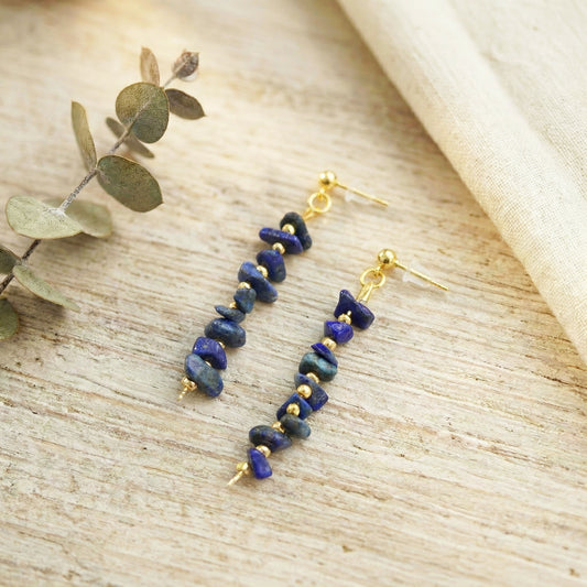 Pair of blue beaded earrings on a wooden surface with a leafy branch.