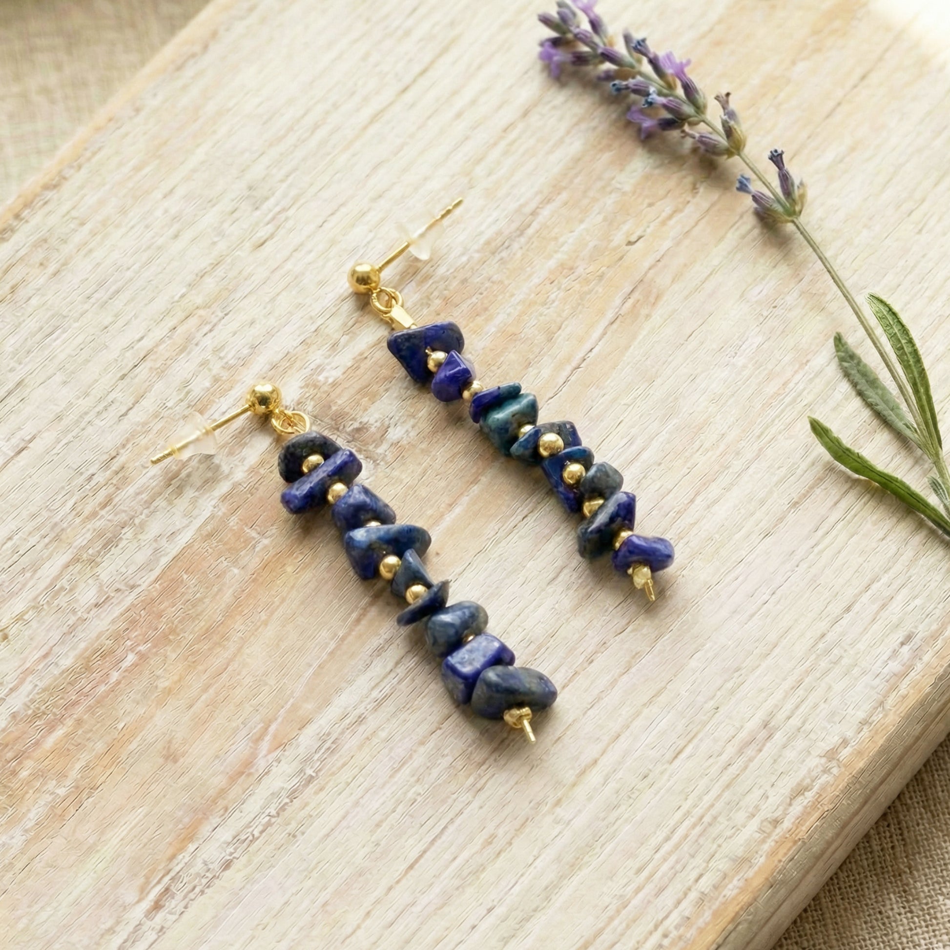 Pair of blue stone earrings with gold accents on a wooden surface with lavender.
