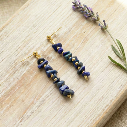 Pair of blue stone earrings with gold accents on a wooden surface with lavender.