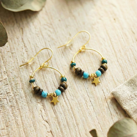 Gold hoop earrings with beads and star charms on a wooden surface