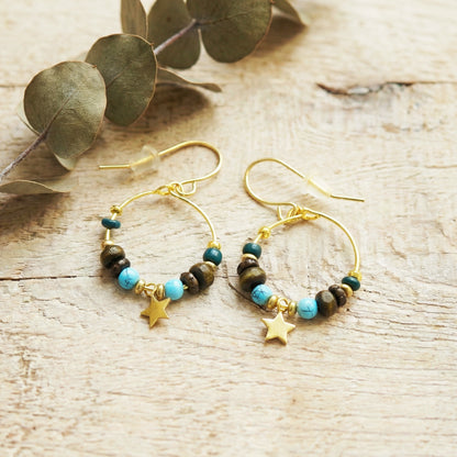Gold hoop earrings with beads and star charms on a wooden surface with eucalyptus leaves.