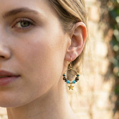 Close-up of a woman wearing a gold hoop earring with turquoise beads and a star charm.