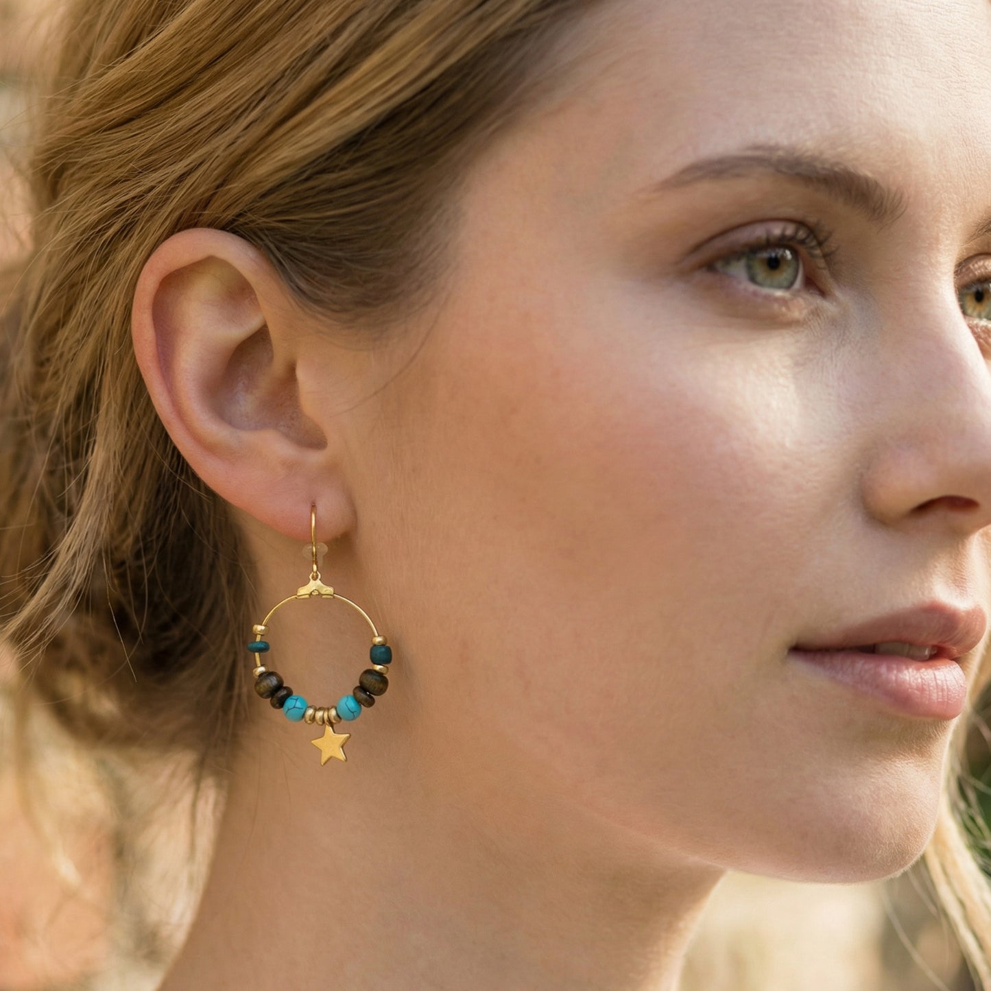 Close-up of a woman wearing gold hoop earrings with beads and a star charm.