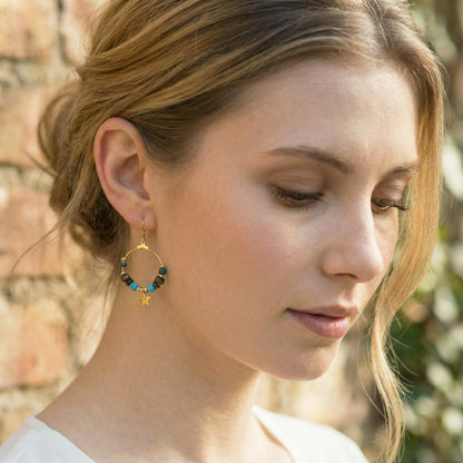 Woman wearing gold hoop earrings with beads and a star, outdoors.