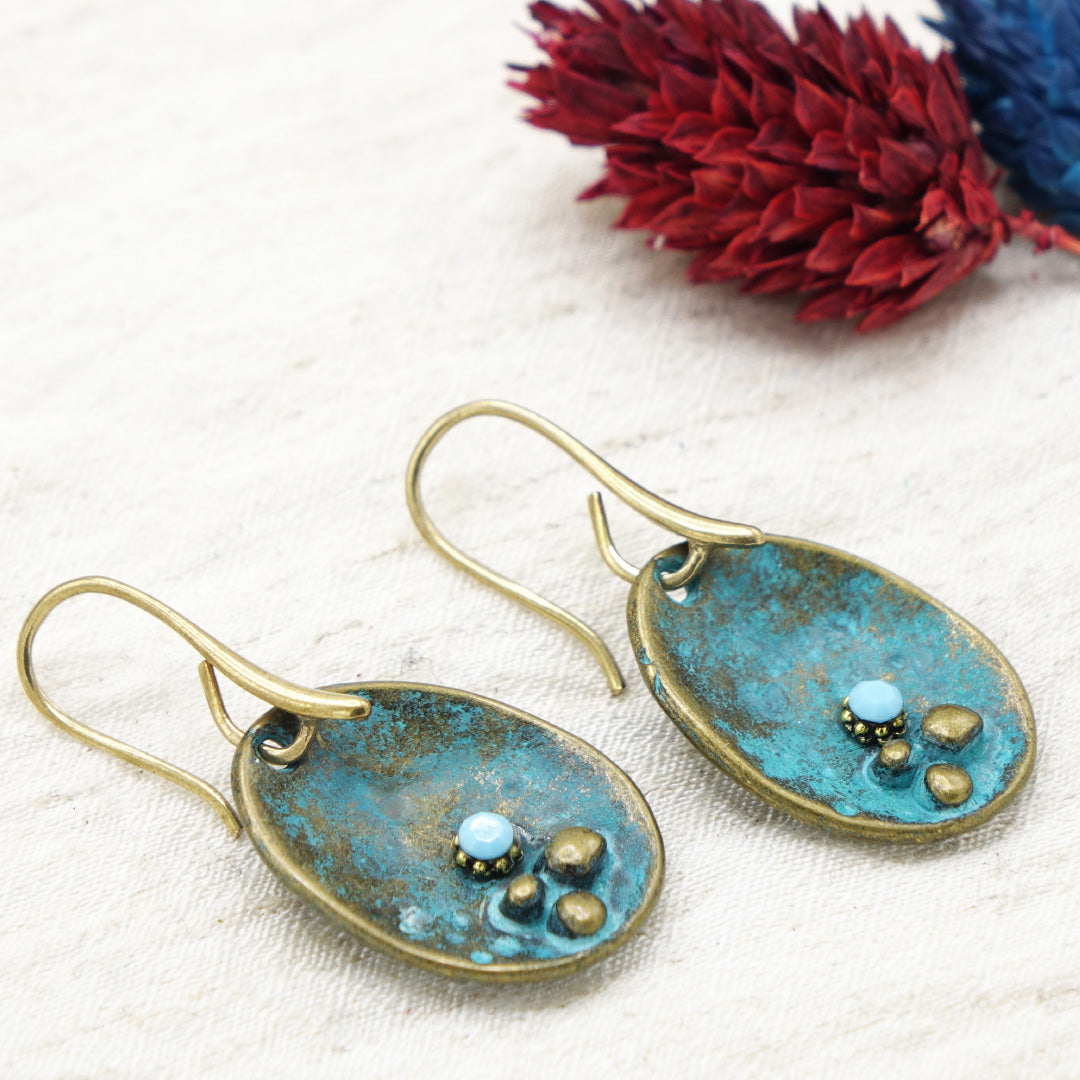 Pair of blue and gold earrings on a white fabric background with red flowers.