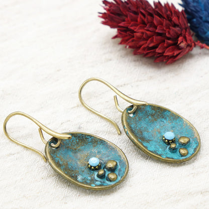 Pair of blue and gold earrings on a white fabric background with red flowers.