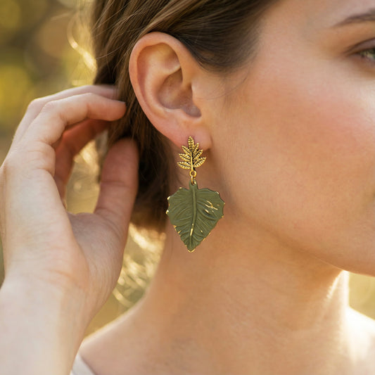 Close-up of a person wearing leaf-shaped earrings with a blurred natural background