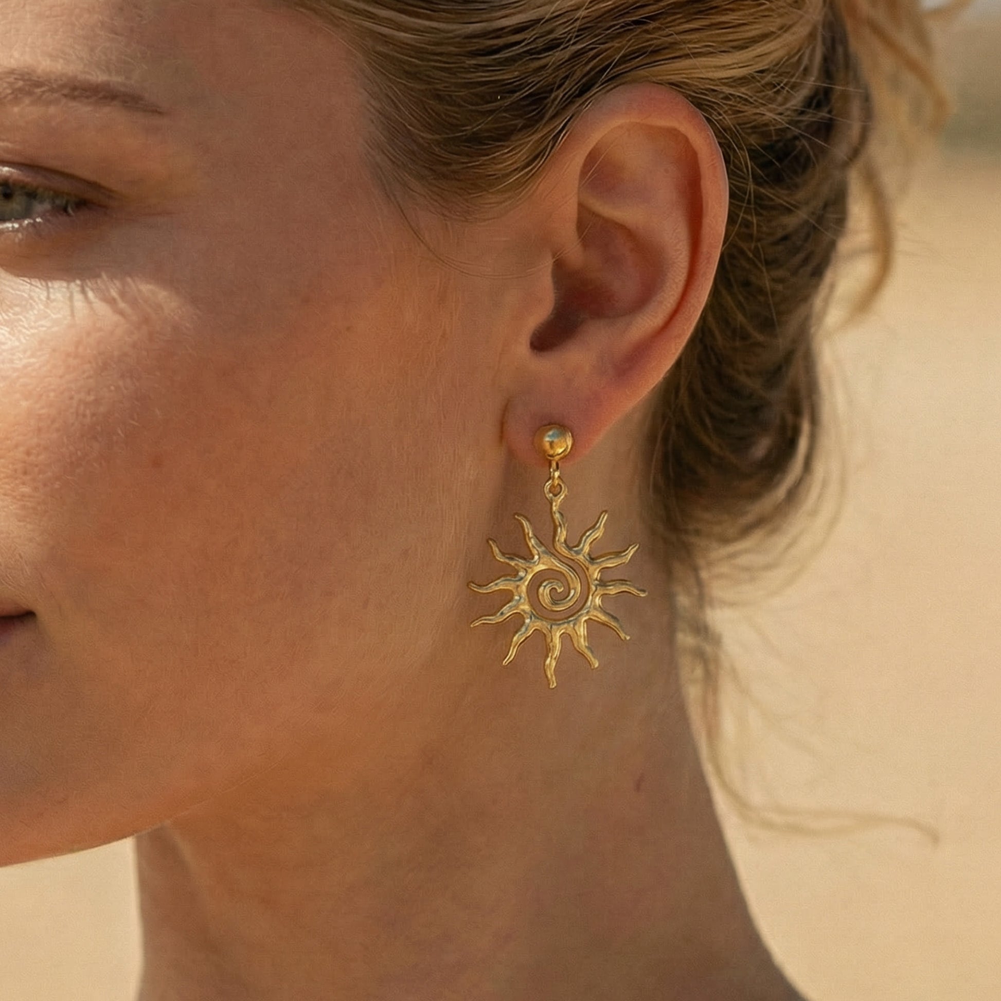 Close-up of a woman wearing gold sun-shaped earrings against a neutral background