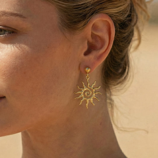 Close-up of a woman wearing gold sun-shaped earrings against a neutral background