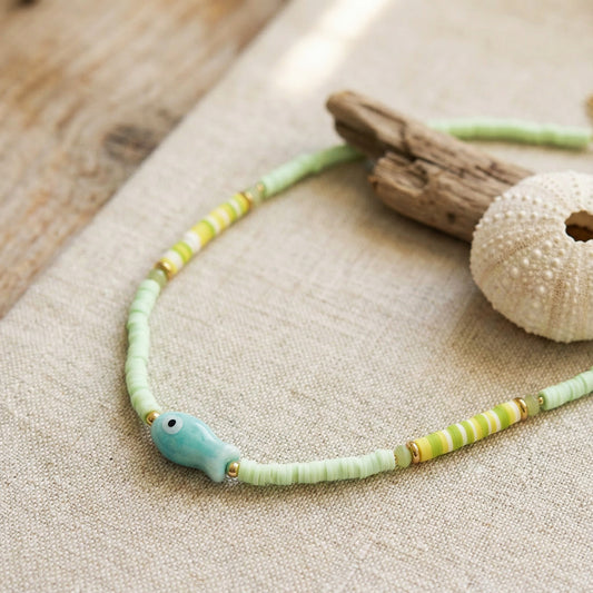 Necklace with green and yellow beads and a blue fish charm on a wooden surface.