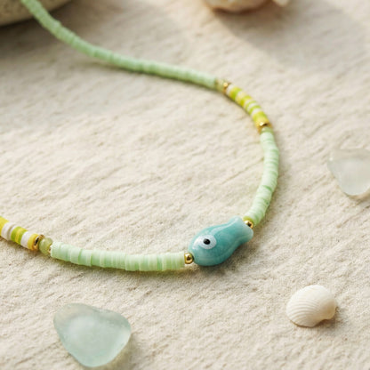Necklace with green beads and a blue pendant on a sandy surface