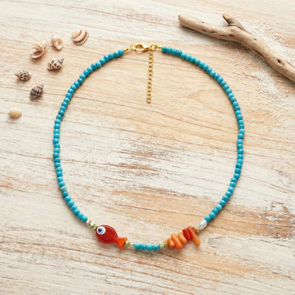 Necklace with blue beads and a fish charm on a wooden surface with shells.
