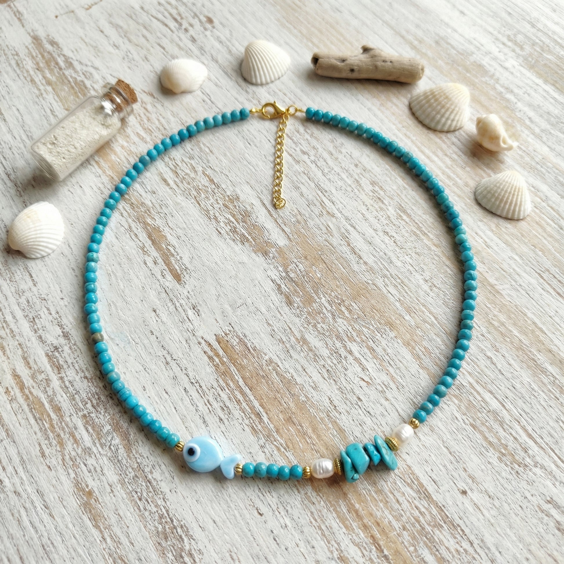 Turquoise beaded necklace with pearls on a wooden surface with shells and a bottle.