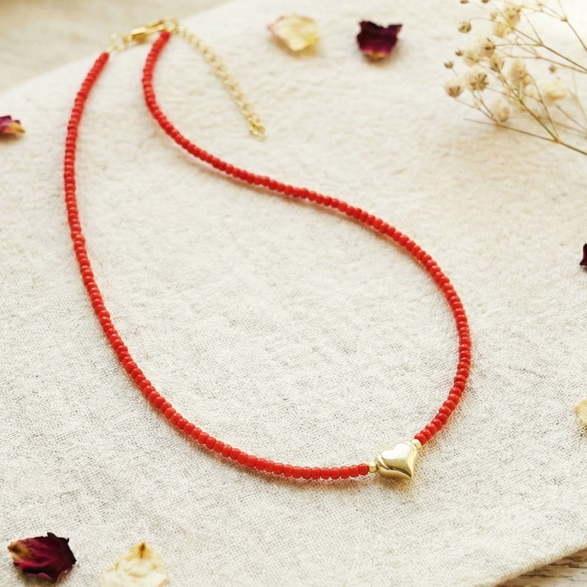Red beaded necklace with a gold heart pendant on a light background