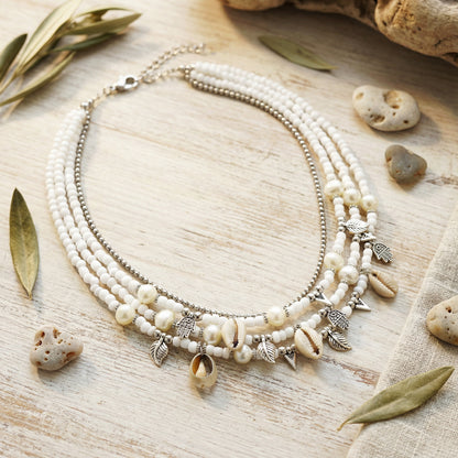 Necklace with shell and leaf charms on a wooden surface with leaves and stones