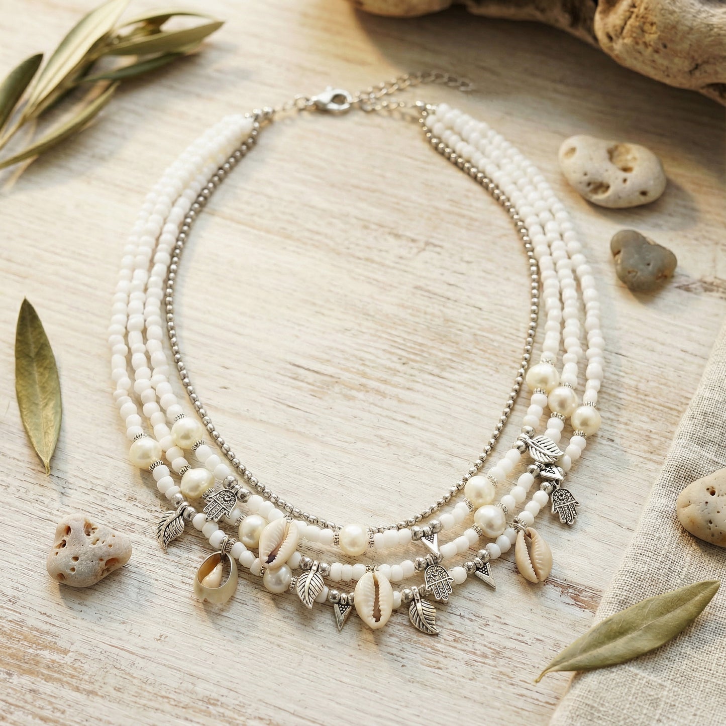 Necklace with shell and leaf charms on a wooden surface with leaves and stones.