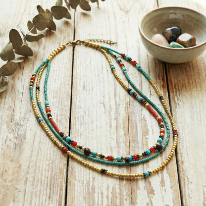 Colorful beaded necklace on a wooden surface with a bowl of stones and leaves.