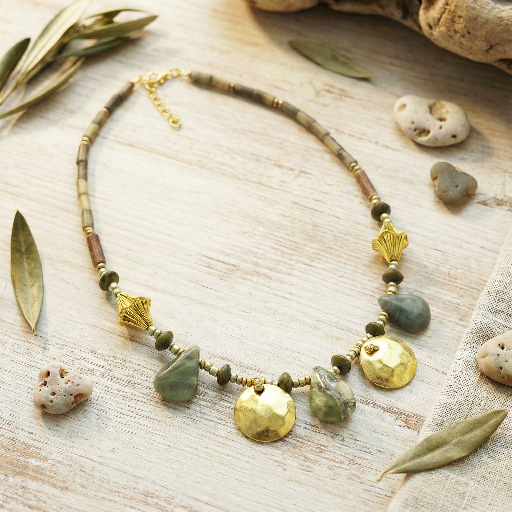 Necklace with natural stones and gold accents on a wooden surface with leaves and stones.