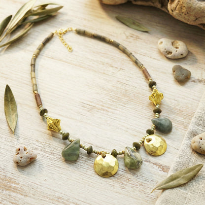 Necklace with natural stones and gold accents on a wooden surface with leaves and stones.