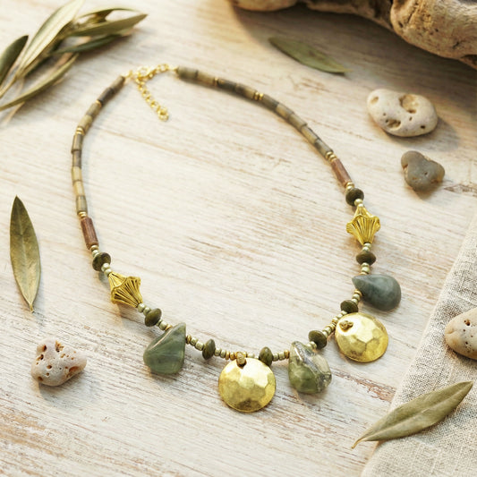Necklace with natural stones and gold accents on a wooden surface with leaves and stones.