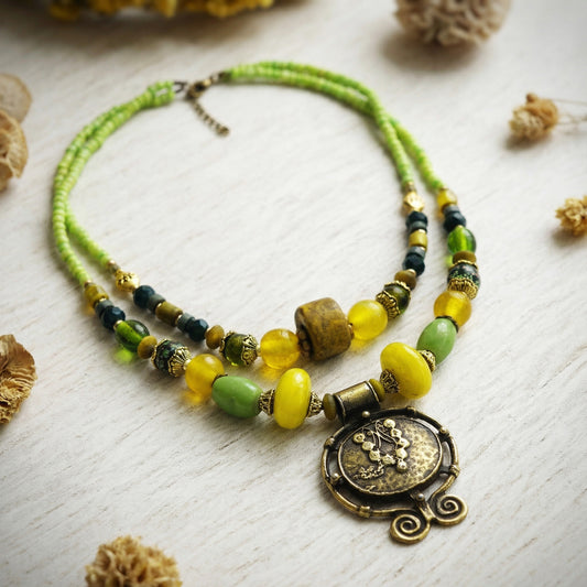 Necklace with green and yellow beads and a decorative pendant on a light wooden surface.