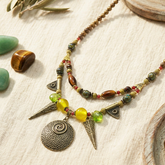 Necklace with beads and charms on a textured surface with stones and leaves.
