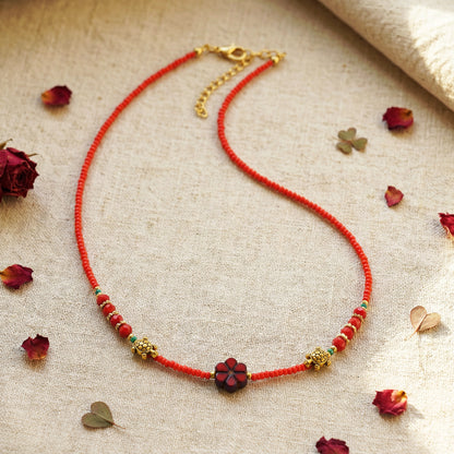 Red beaded necklace with gold accents on a beige fabric background
