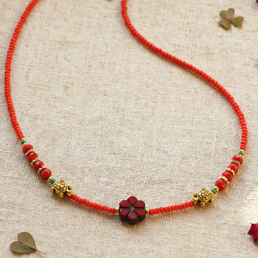 Red beaded necklace with decorative flower pendant on a textured beige background