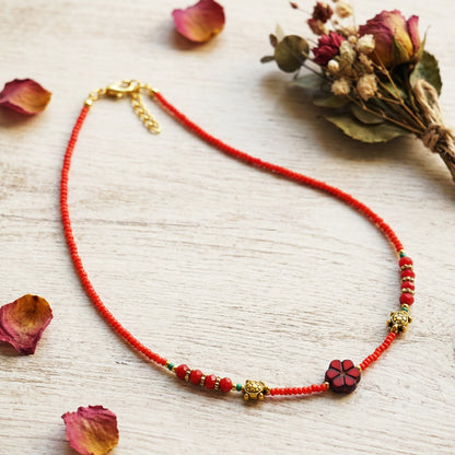 Red beaded necklace with floral elements on a light wooden surface with dried flowers.