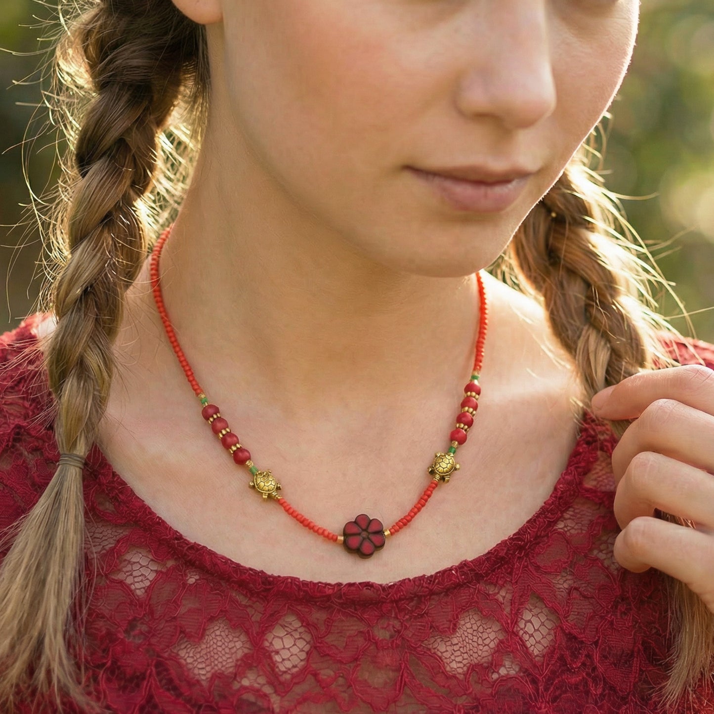 Close-up of a person wearing a red beaded necklace with a floral pendant, outdoors.