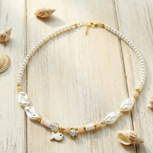 Pearl necklace with gold accents and shell decorations on a wooden surface with seashells.