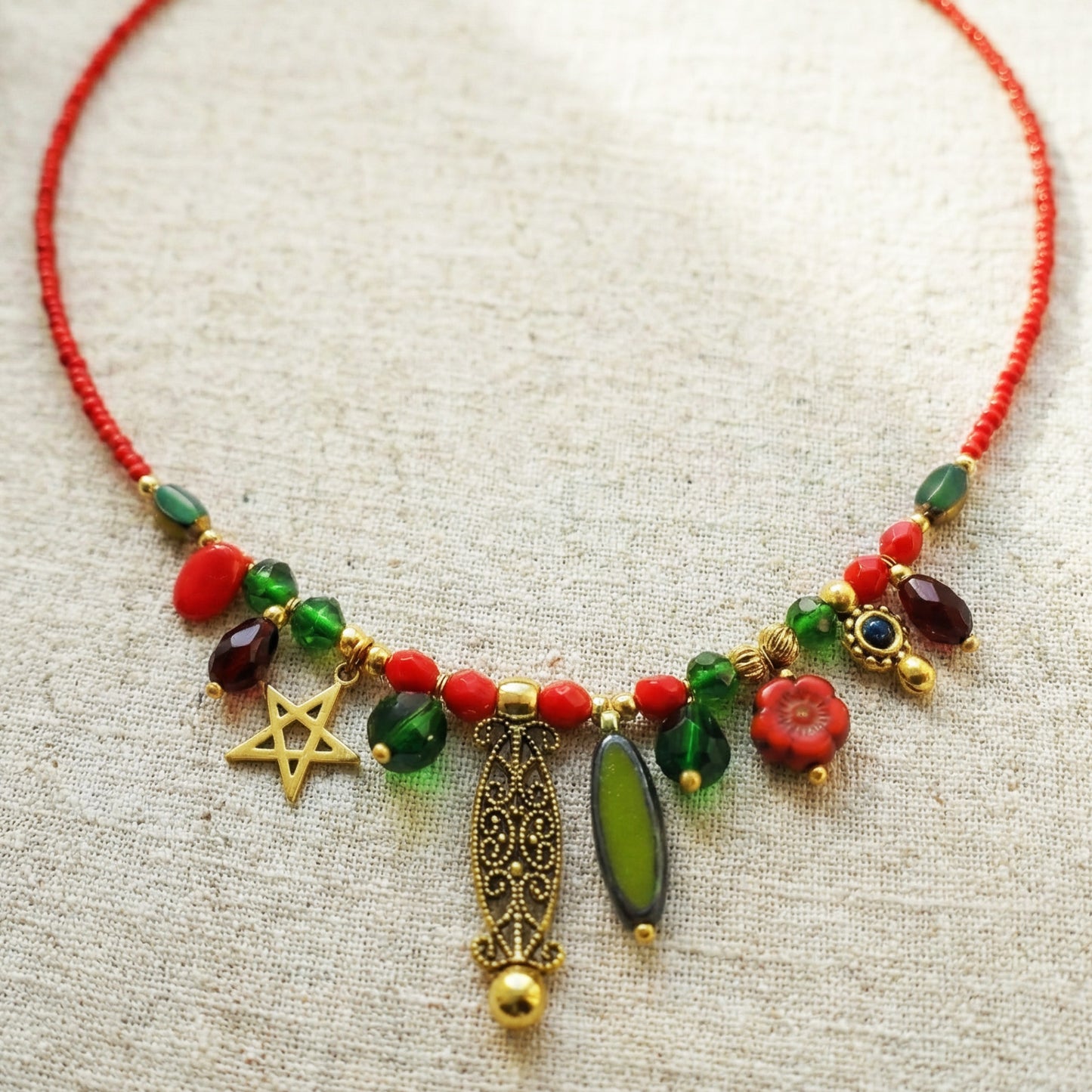 Colorful beaded necklace with gold accents and red thread on a textured beige background